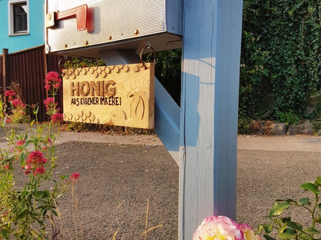 Ein aus Holz geschnitztes Schild am Briefkasten mit der Aufschrift: Honig aus eigener Imkerei.